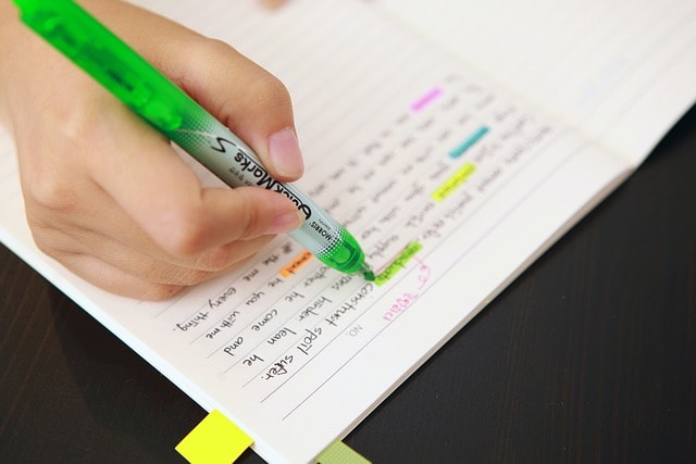 A person using a highlighter on a text written in a notebook.