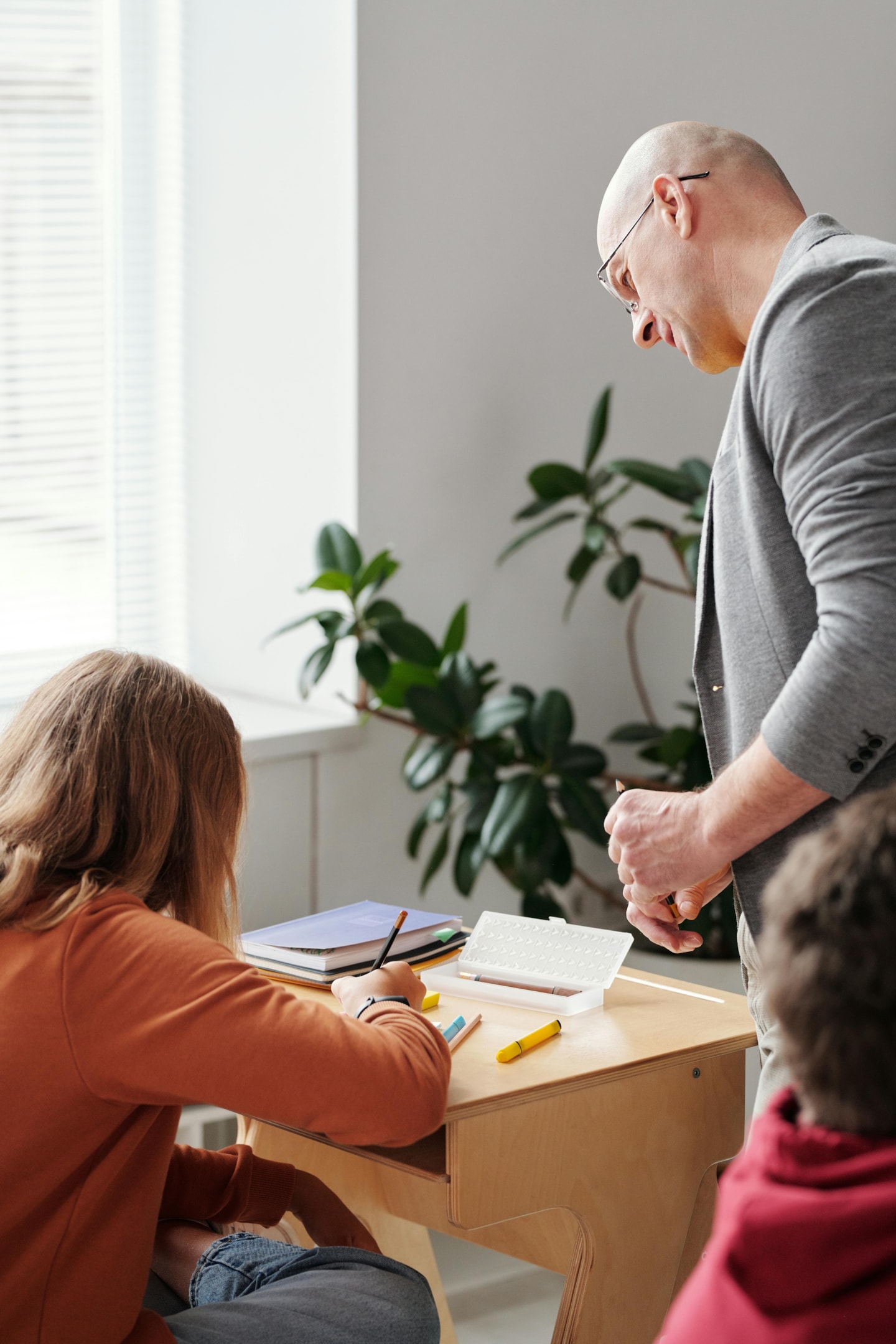 A male teacher looking over the shoulder of a student who is writing. 