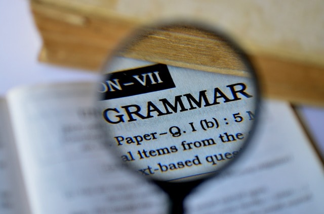 A magnifying glass on top of the word "Grammar" in an open book.