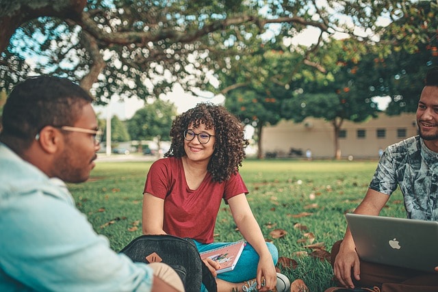 Some students sitting on the grass with one having a laptop on his lap.