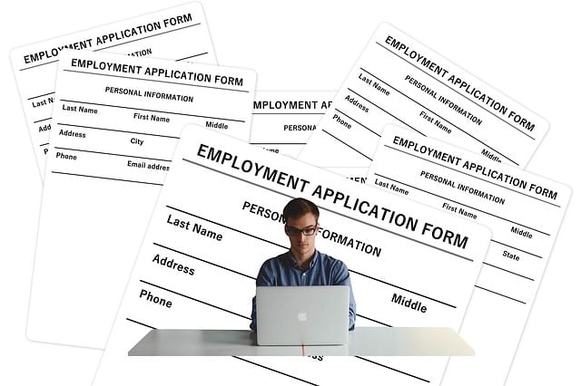 A person working on their laptop and in the background many applications forms spread out.