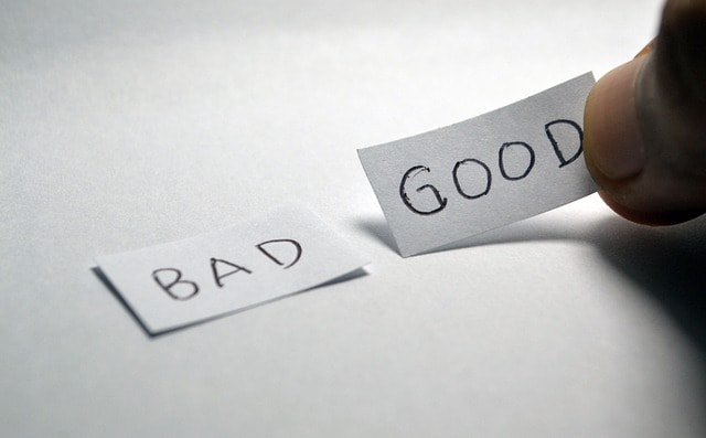 A person placing two pieces of paper saying "bad" and "good" on a white surface.