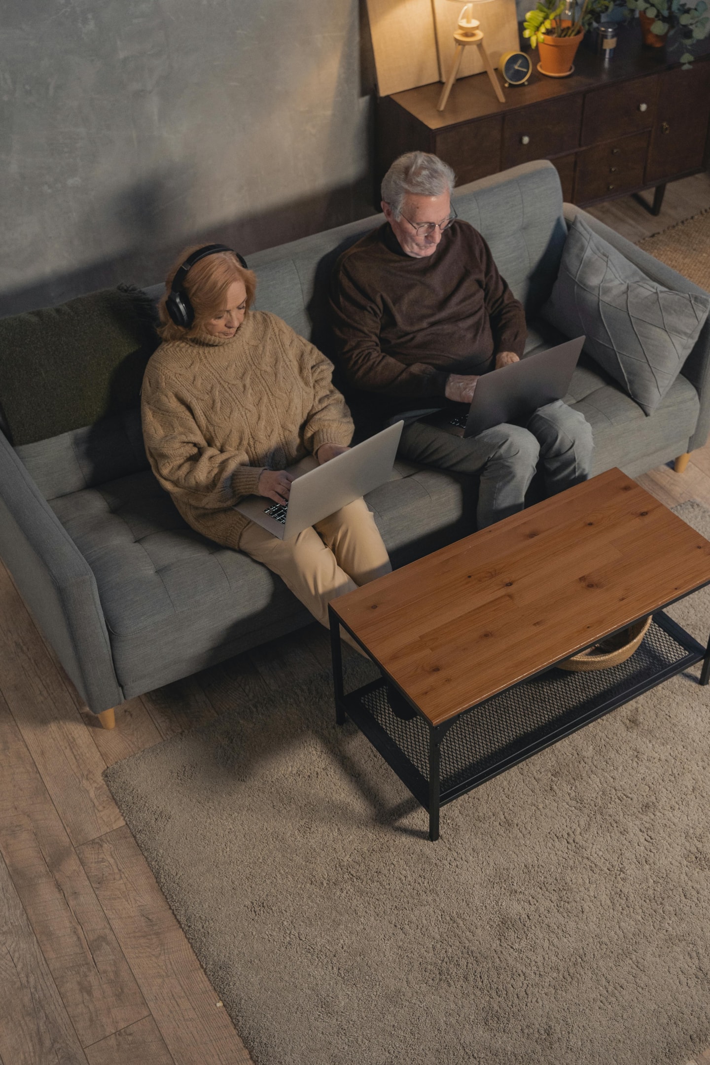 An elderly man and woman sitting on a sofa while using their MacBooks.