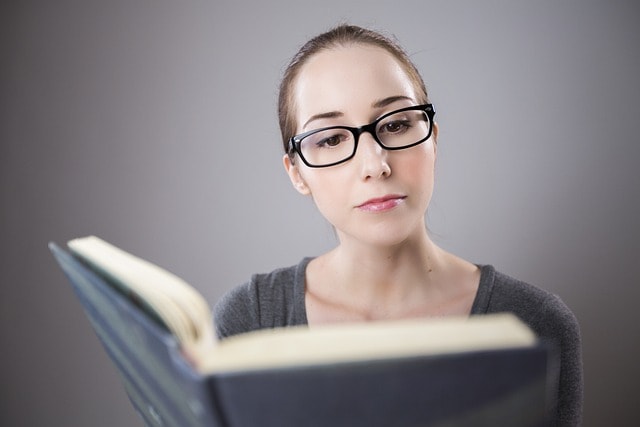 A woman with reading glasses reading a book.