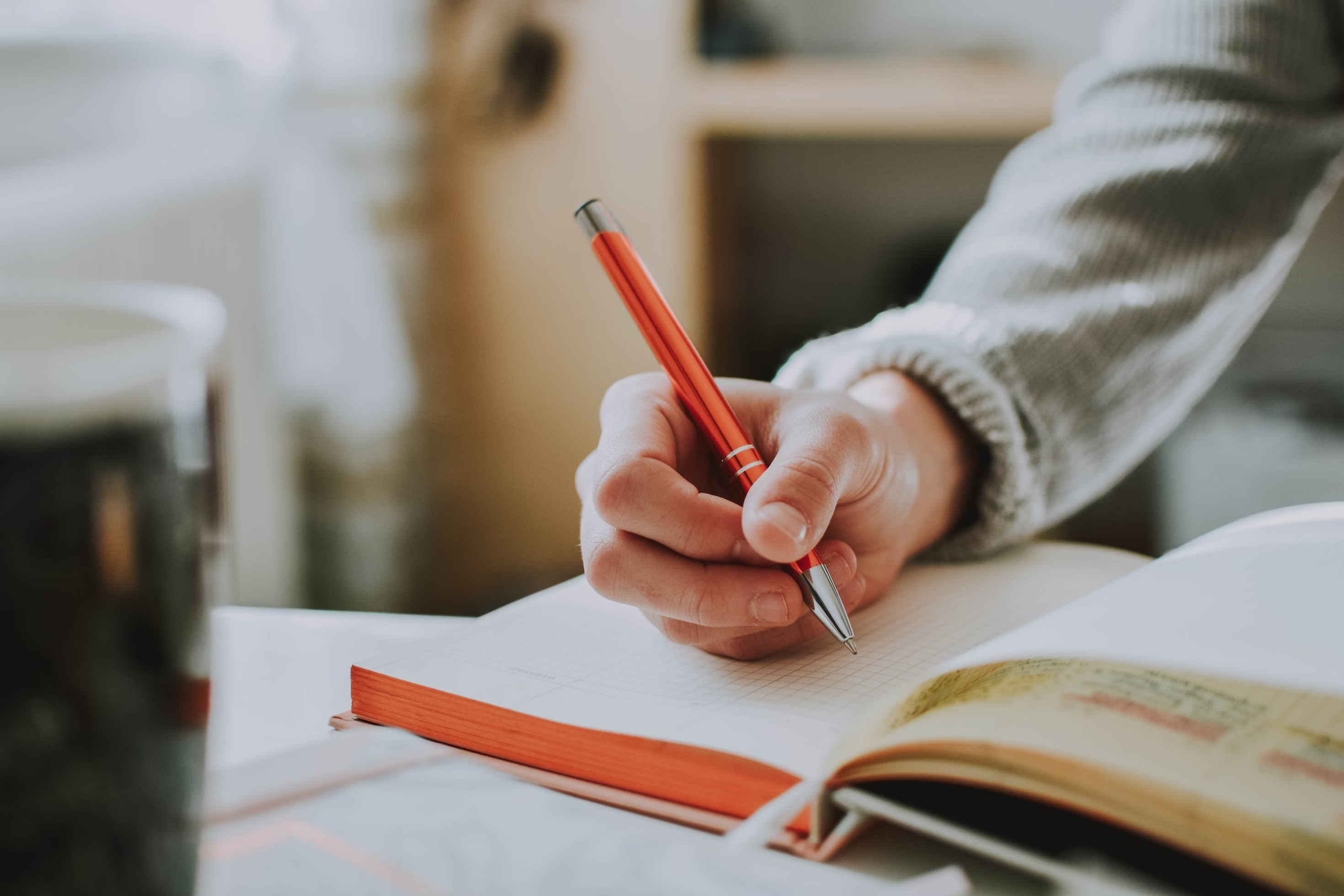 A person holding a red pen over an open notebook