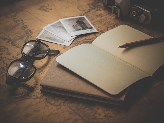 A pair of reading glasses, a notebook, and a pencil on a wooden desk.