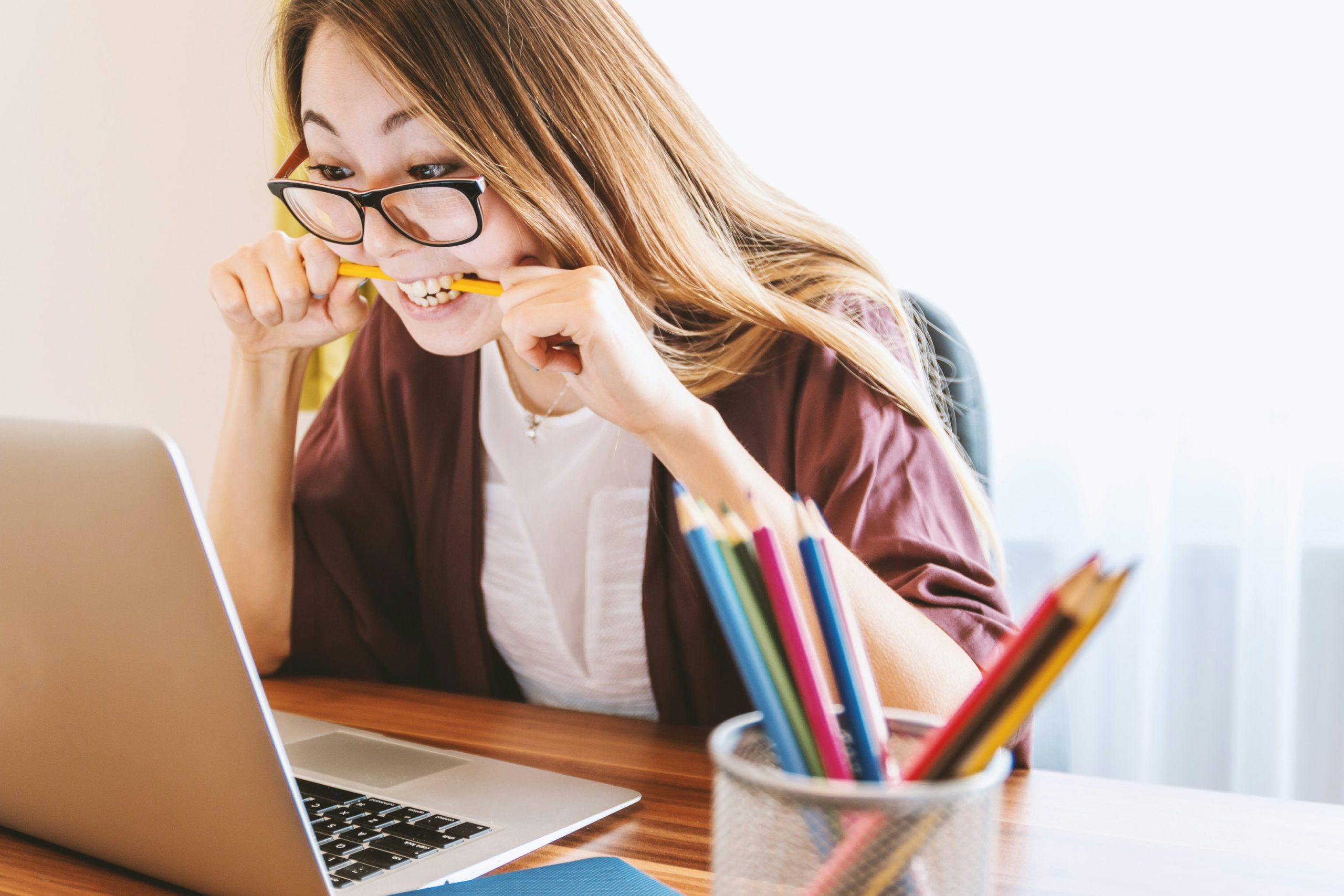 A woman biting a pencil while sitting on chair and looking at a laptop.