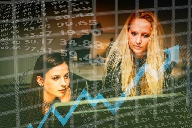 Two women behind a transparent screen displaying numbers and a graph.