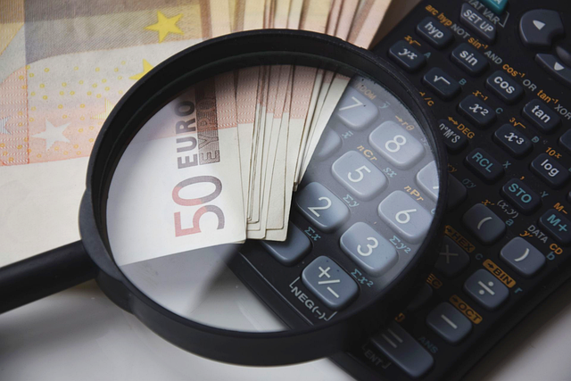 A maglifying glass on top of a calculator and 50 euro notes.