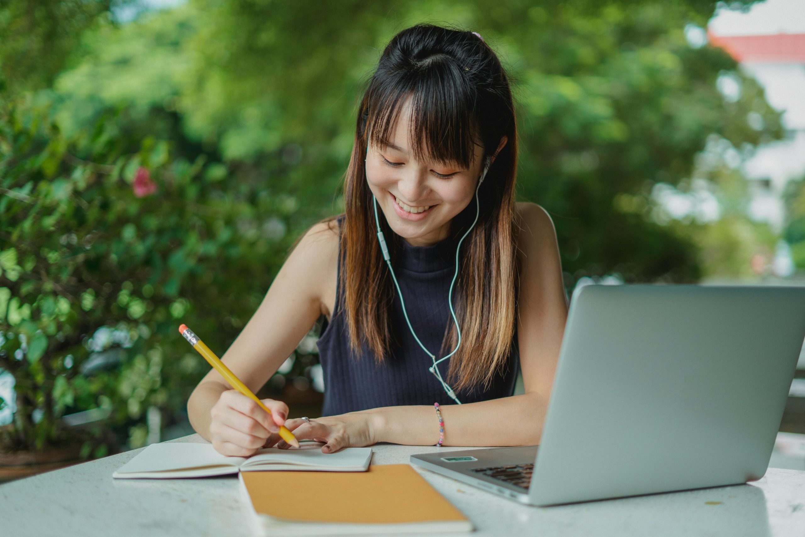 A young woman listens to music with headphones whilst writing on her notepad. 