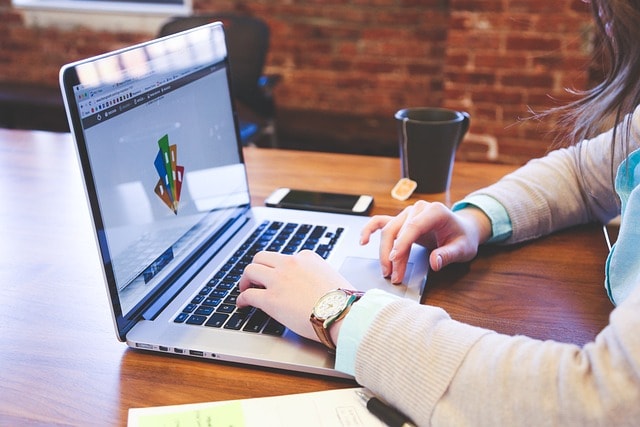 A woman typing on her laptop with a cup of coffee and a smartphone next to her.