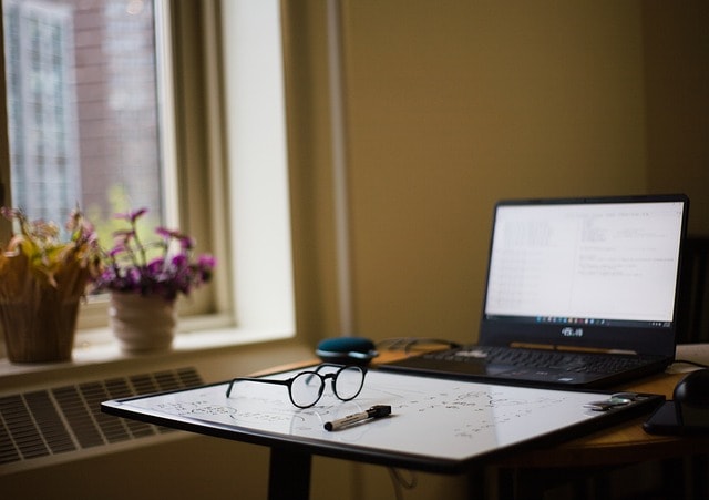 A laptop with a clipboard and balck glasses in front of it.