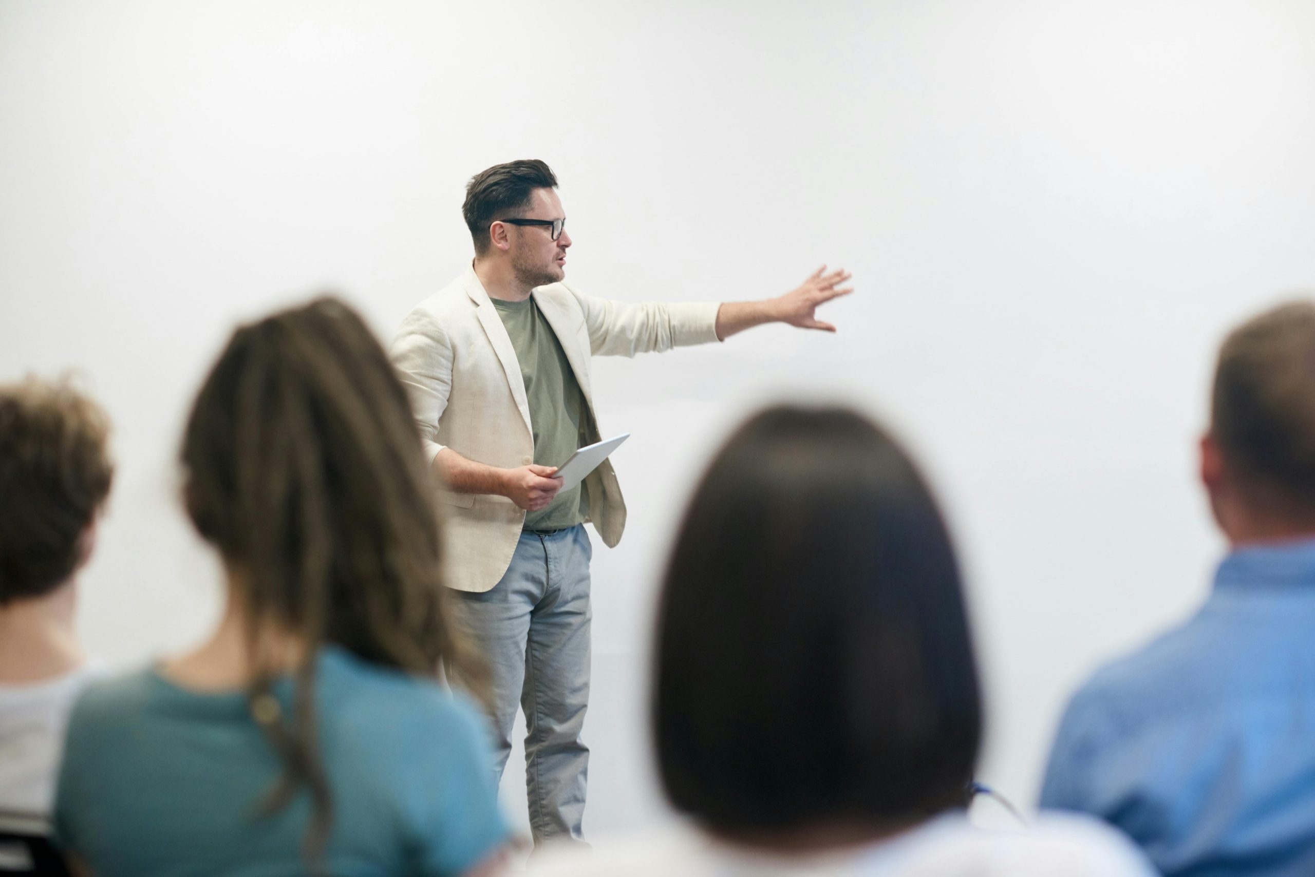 Man in a beige blazer pointing at a board while teaching students. 