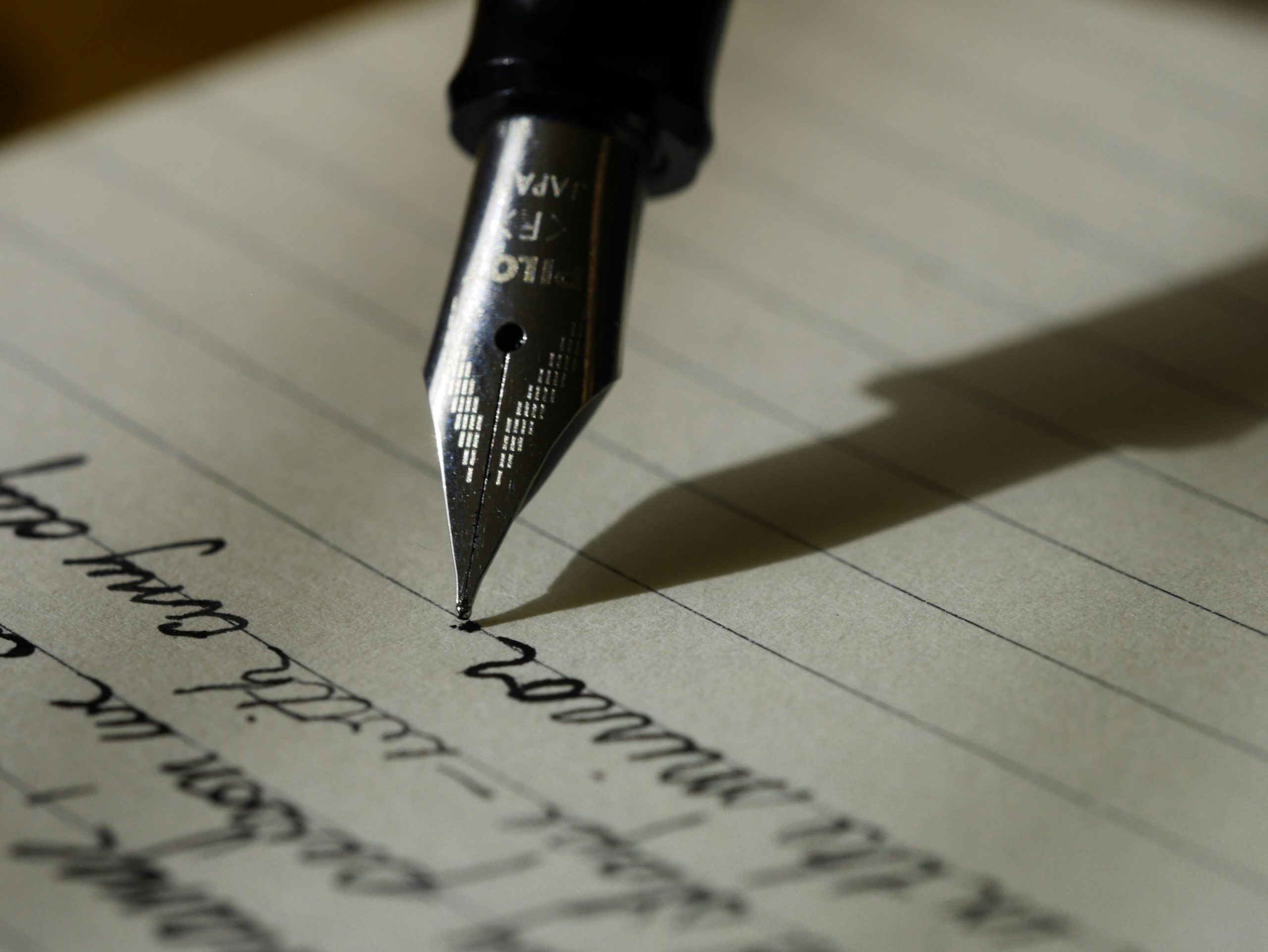 A black fountain pen writing notes on black lined paper. 