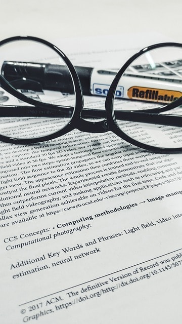 A pair of black reading glasses and a marker on top of a book.