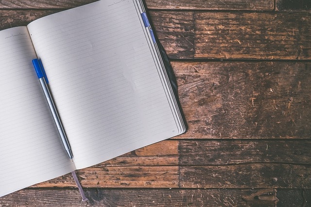 A notebook with two blank pages and a pen on a wooden surface.