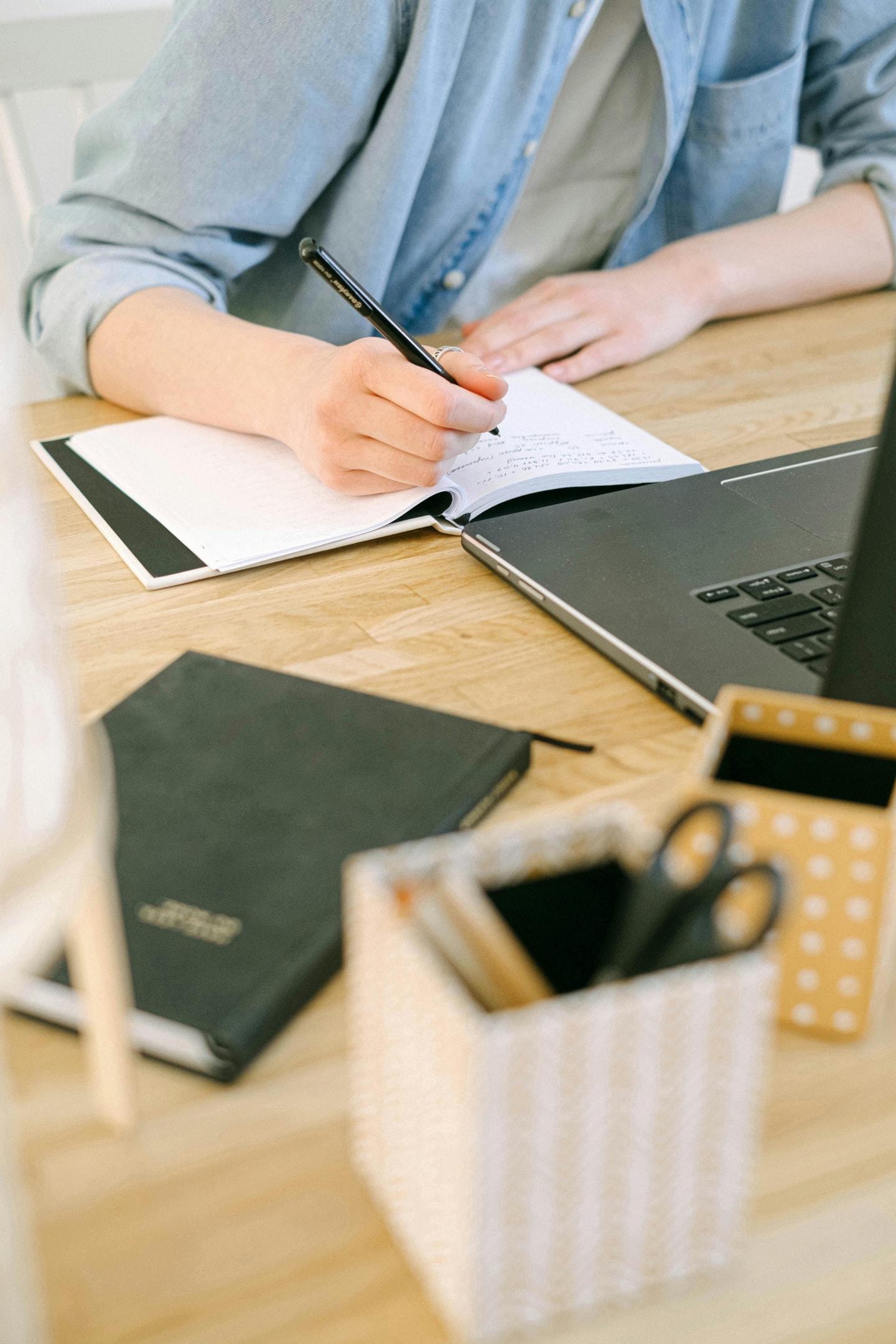 Un estudiant escrivint en un escriptori davant d'un ordinador portàtil.