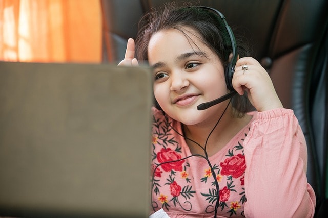 A little girl with headphones sitting in front of a laptop.