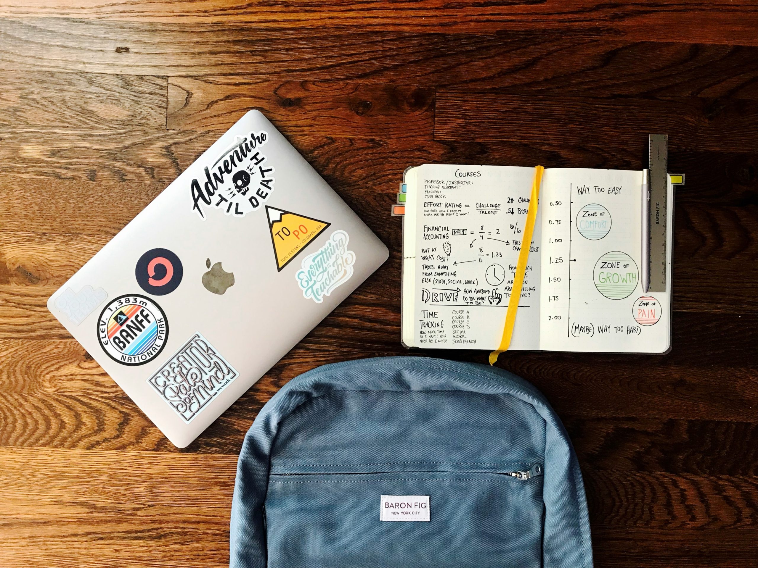 A backpack with a laptop, open notepad, a ruler, and a pen.