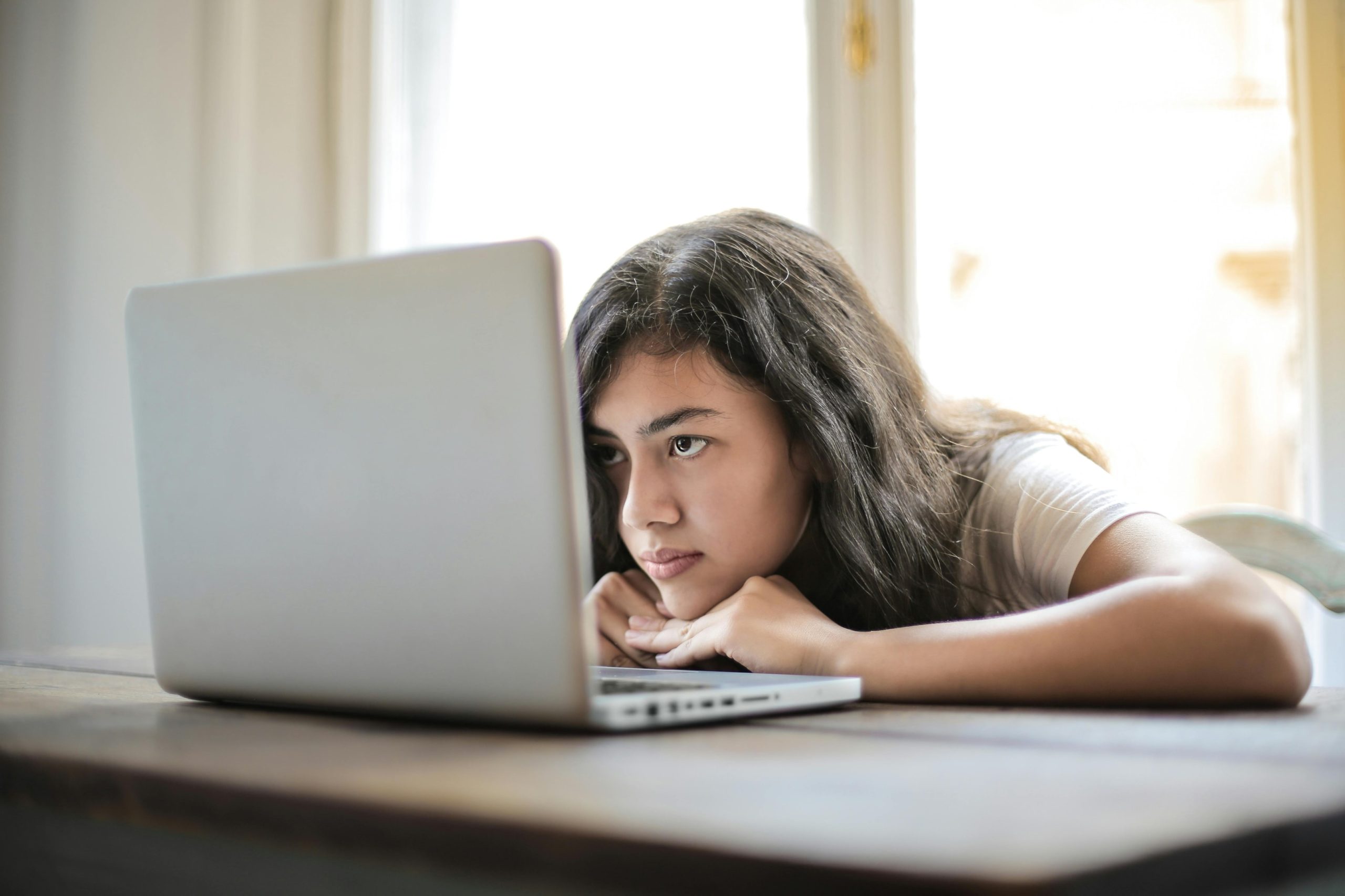 A young woman resting her face on her laptop keyboard. 