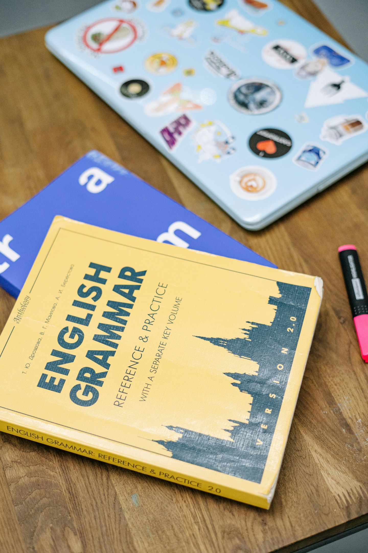 Books on English Grammar and a laptop on a brown wooden table. 