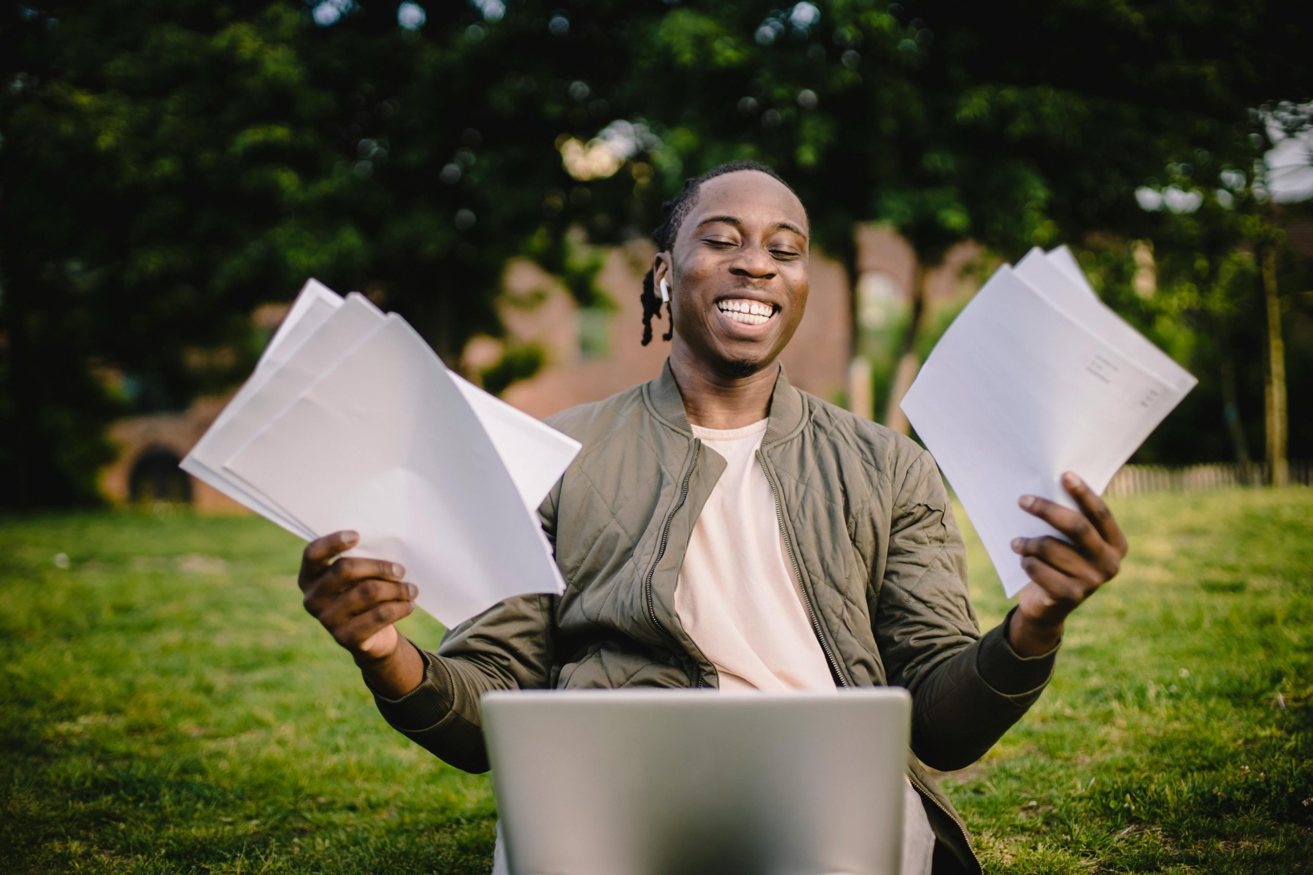 A student with documents and a laptop is smiling joyfully.