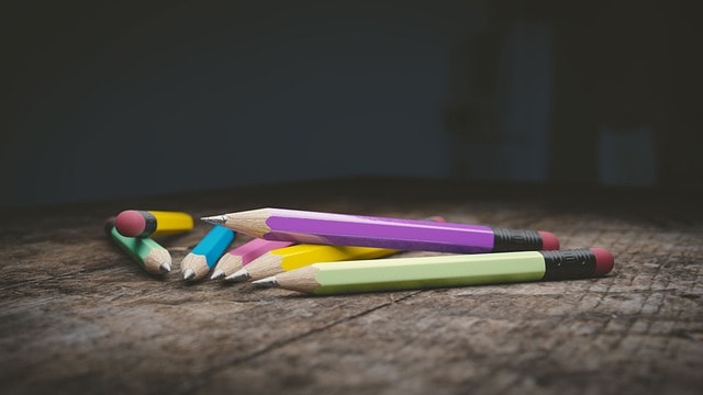 Lots of pencils on top of each other on a wooden surface.