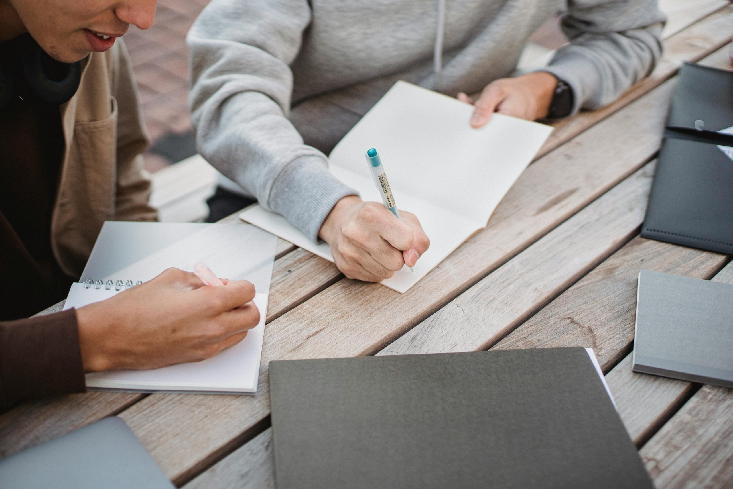 Two male students sitting together writing essays in notebooks. 