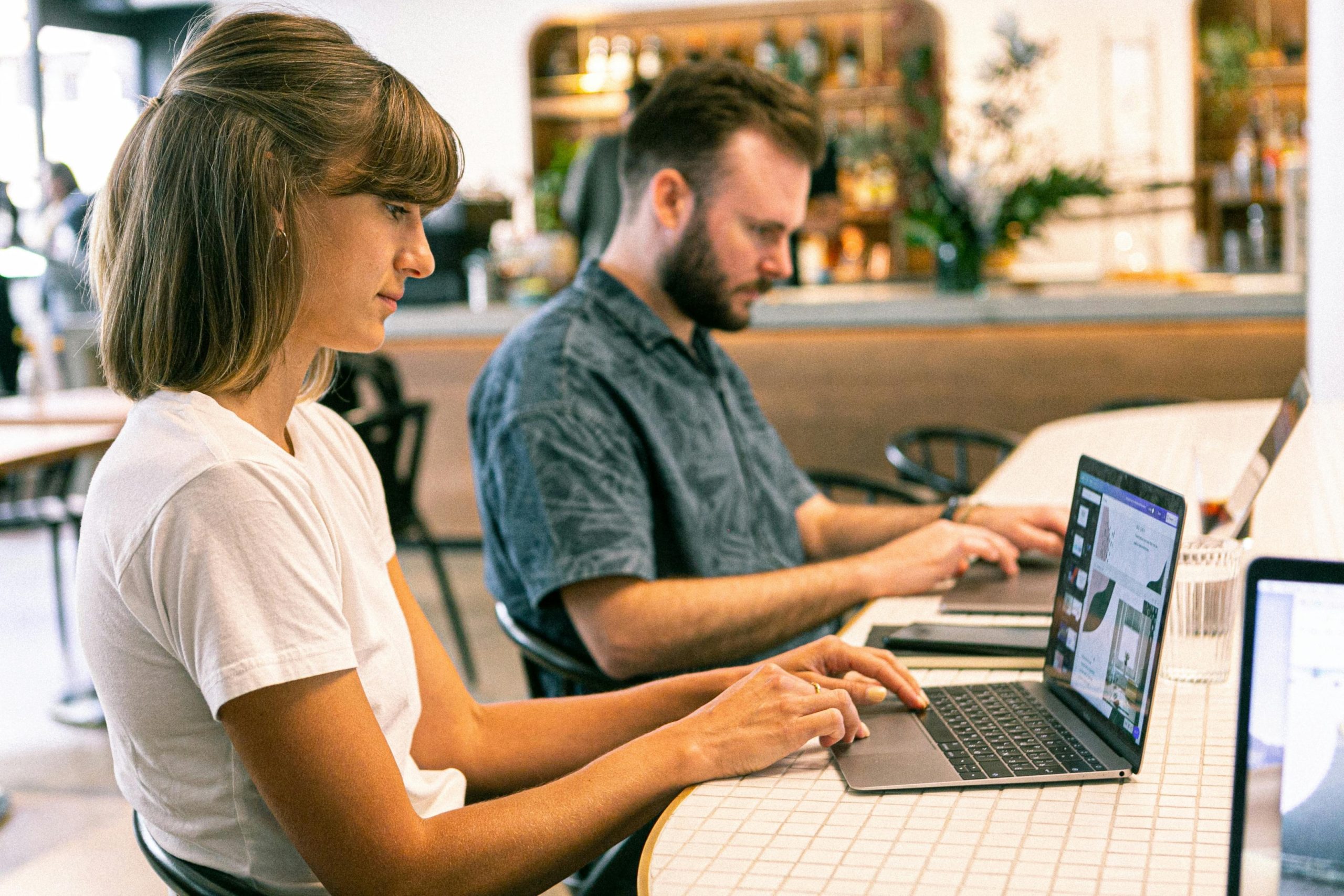 A man and a woman are working side by side on their laptops in a library. 