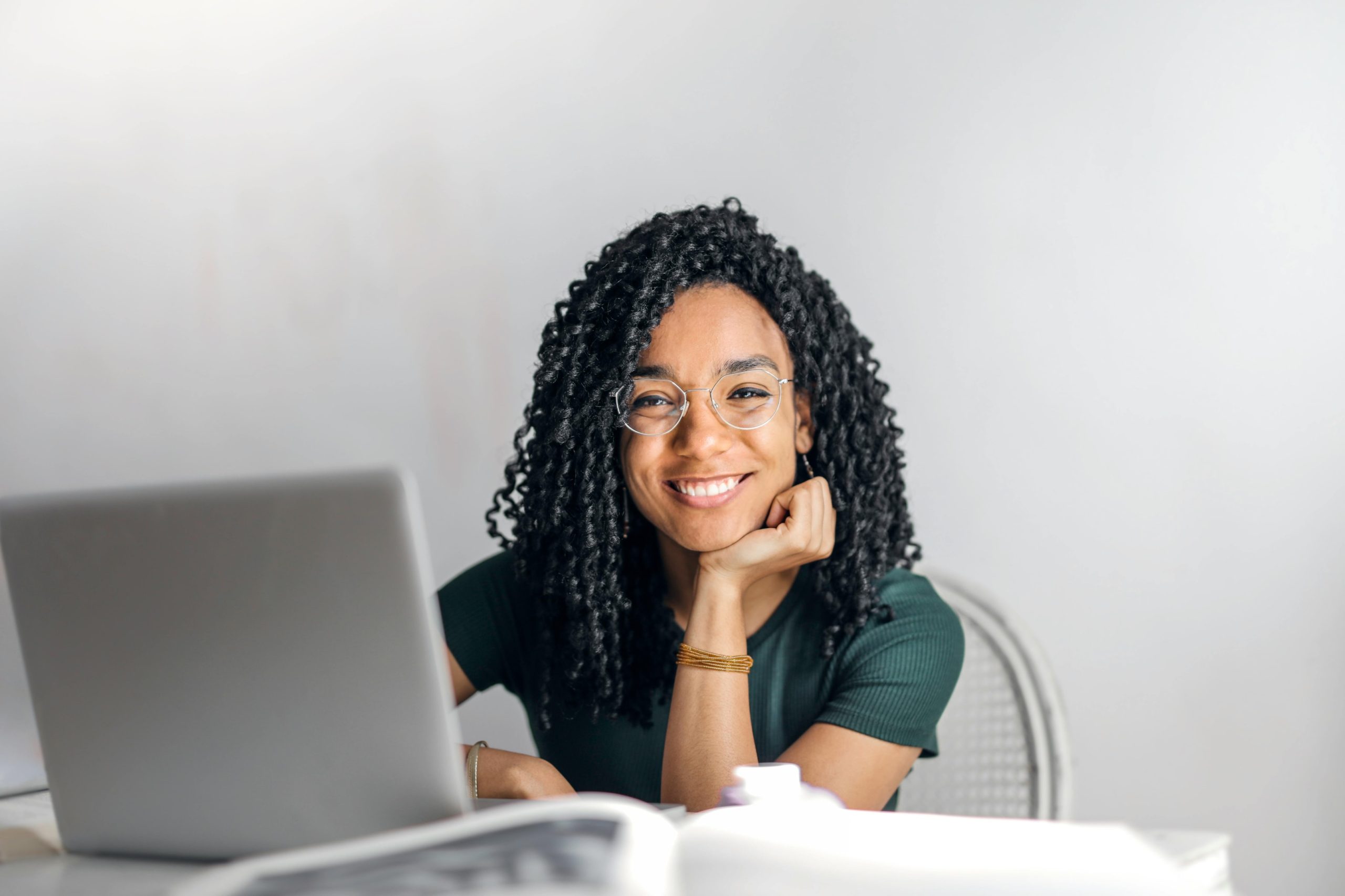 A woman sitting at a desk using a MacBook and smiling. 