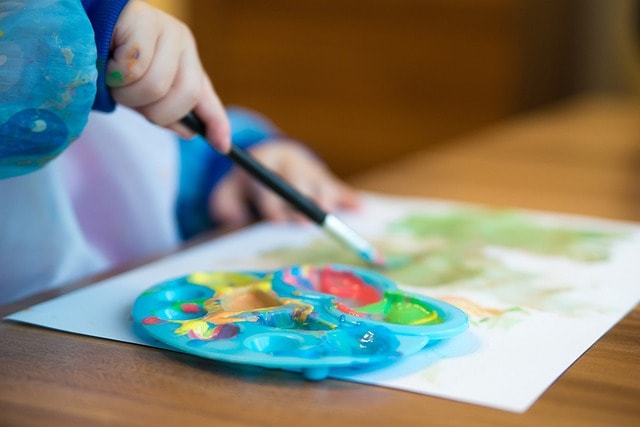 A small child using a color palette to drawn on paper with a paintbrush.