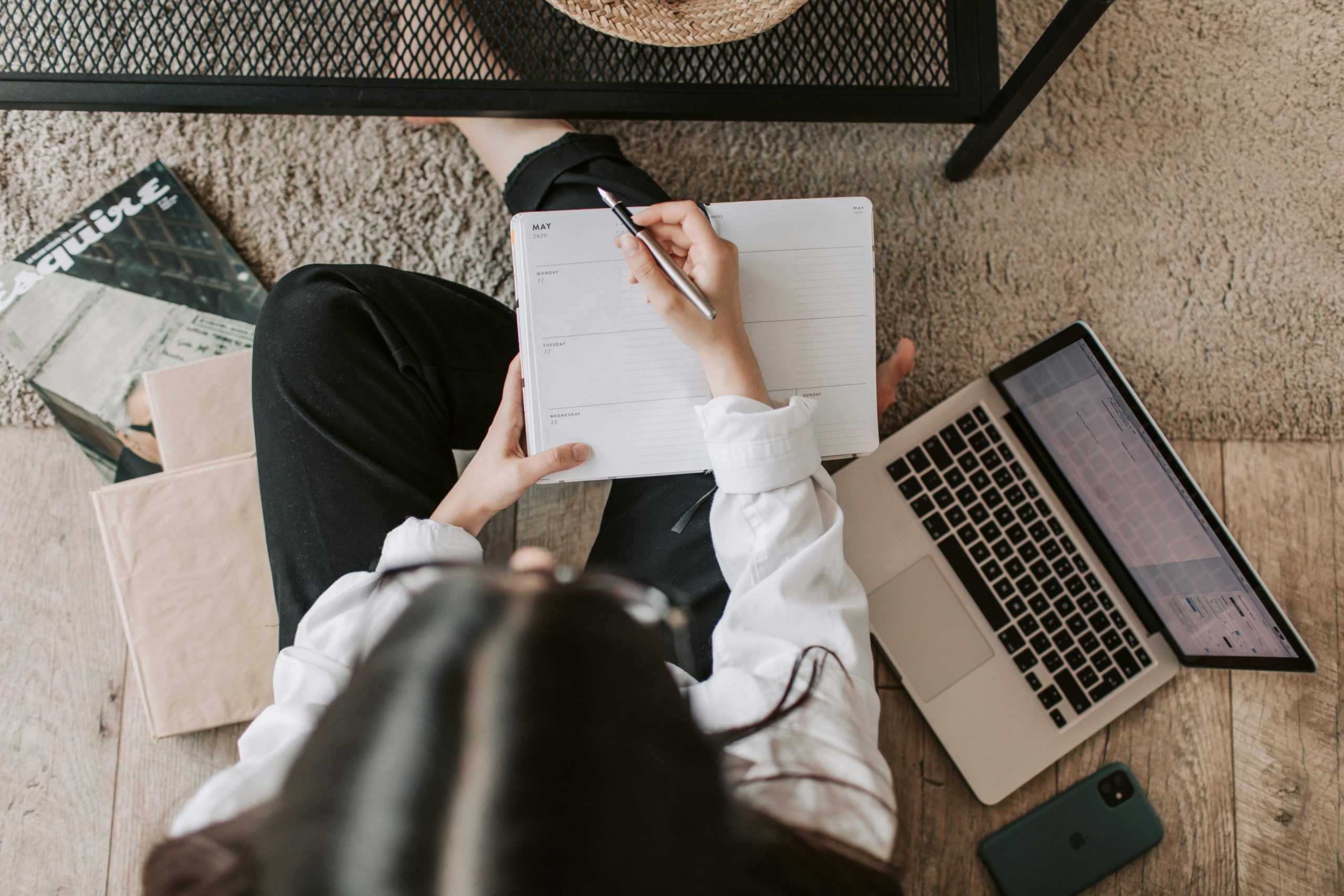 Seorang wanita bekerja di lantai dan mencatat sambil dikelilingi oleh kertas dan laptop.