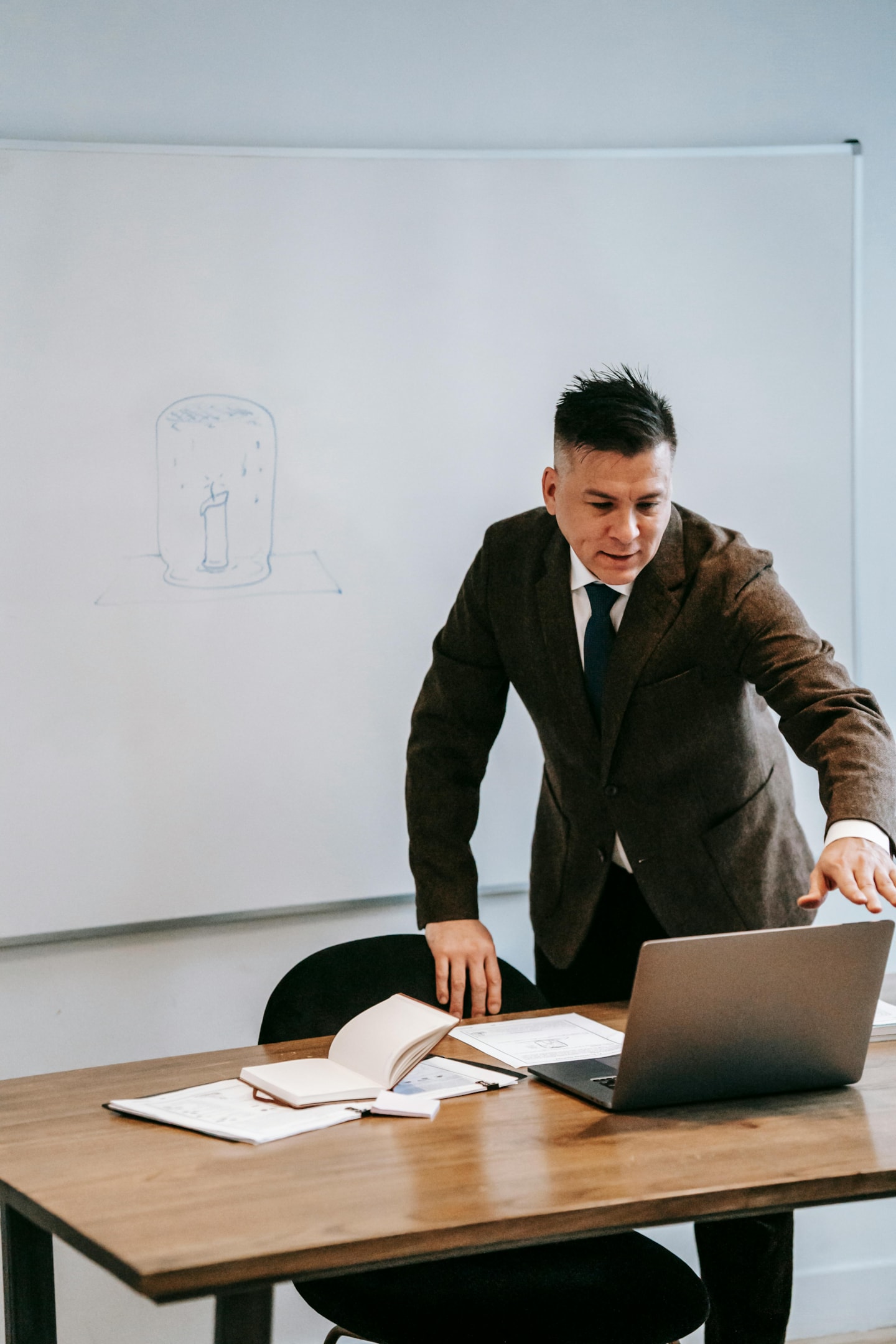 A male teacher standing in front of a laptop in a school classroom. 