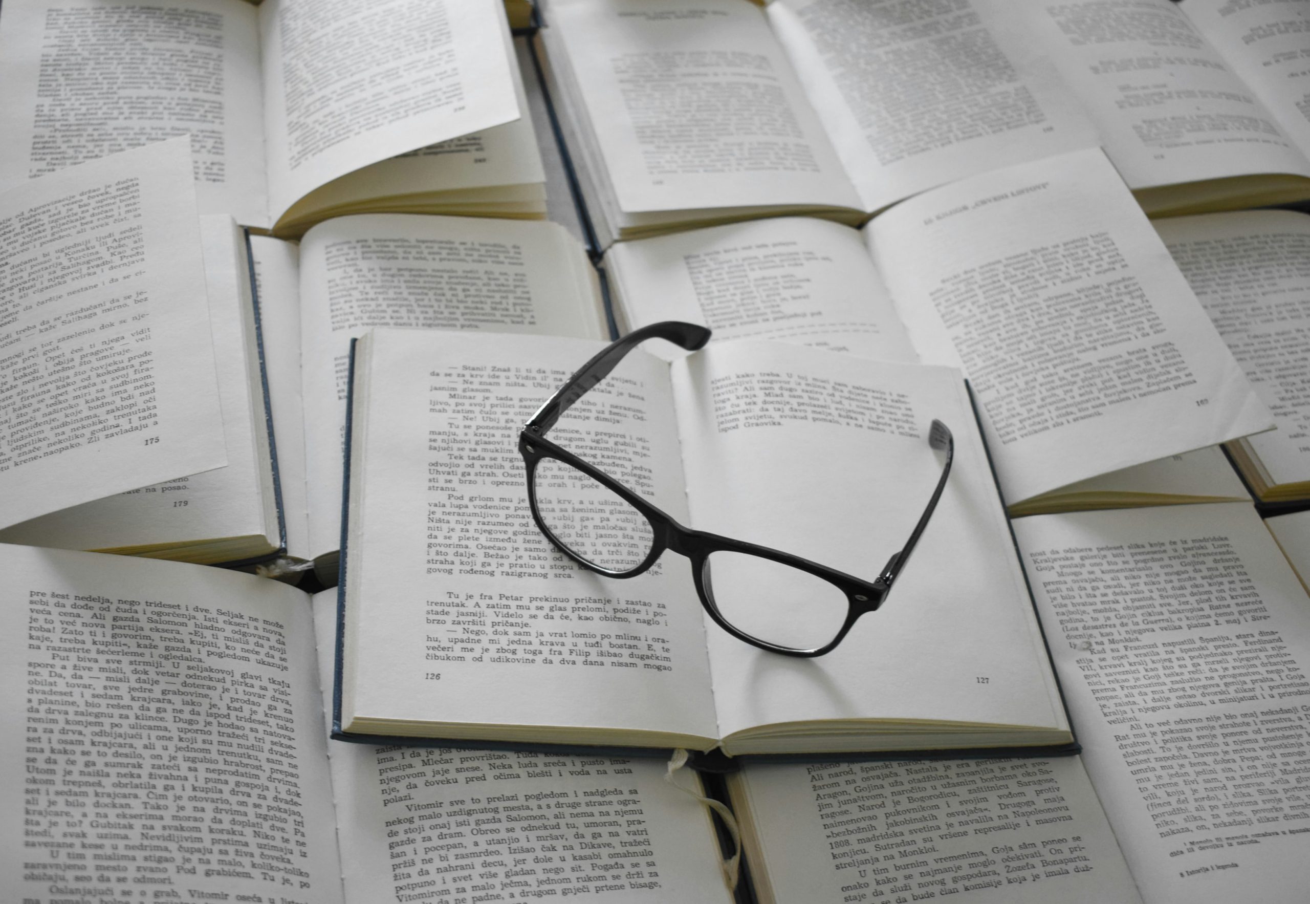 A pair of reading glasses on top of some open books. 