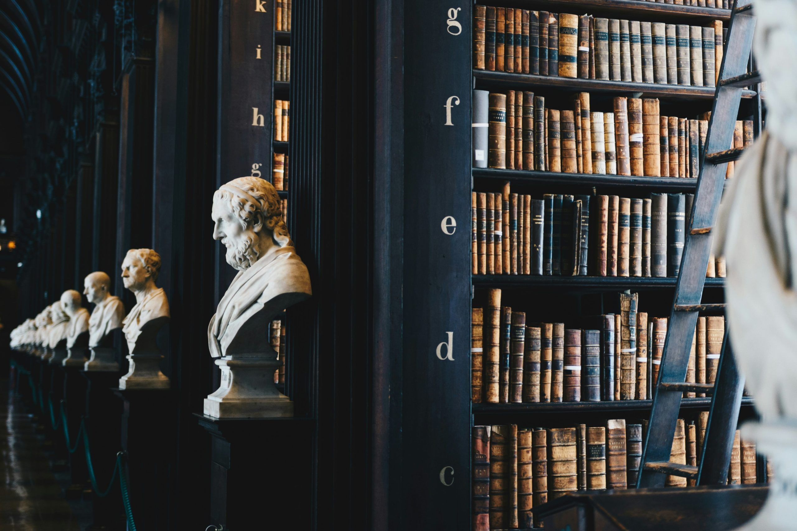 An image of an academic library with black bookcases that have the letters of the alphabet along with many books, and sculptures.