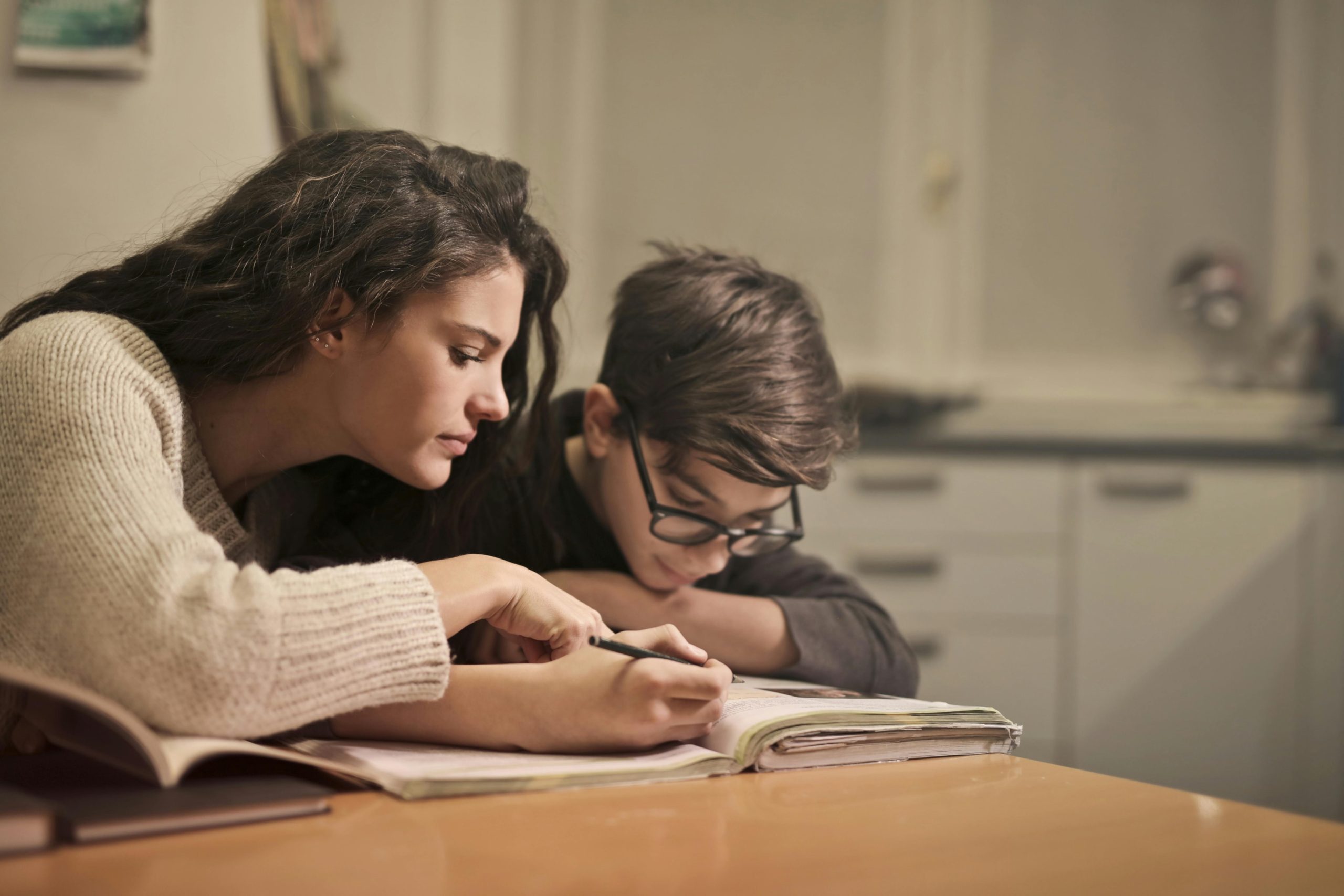  A woman is helping a young boy with homework at home.