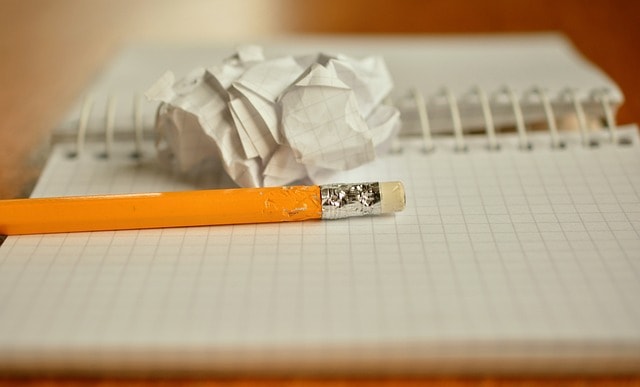 A pencil on top of a notebook next to a crumpled piece of paper.