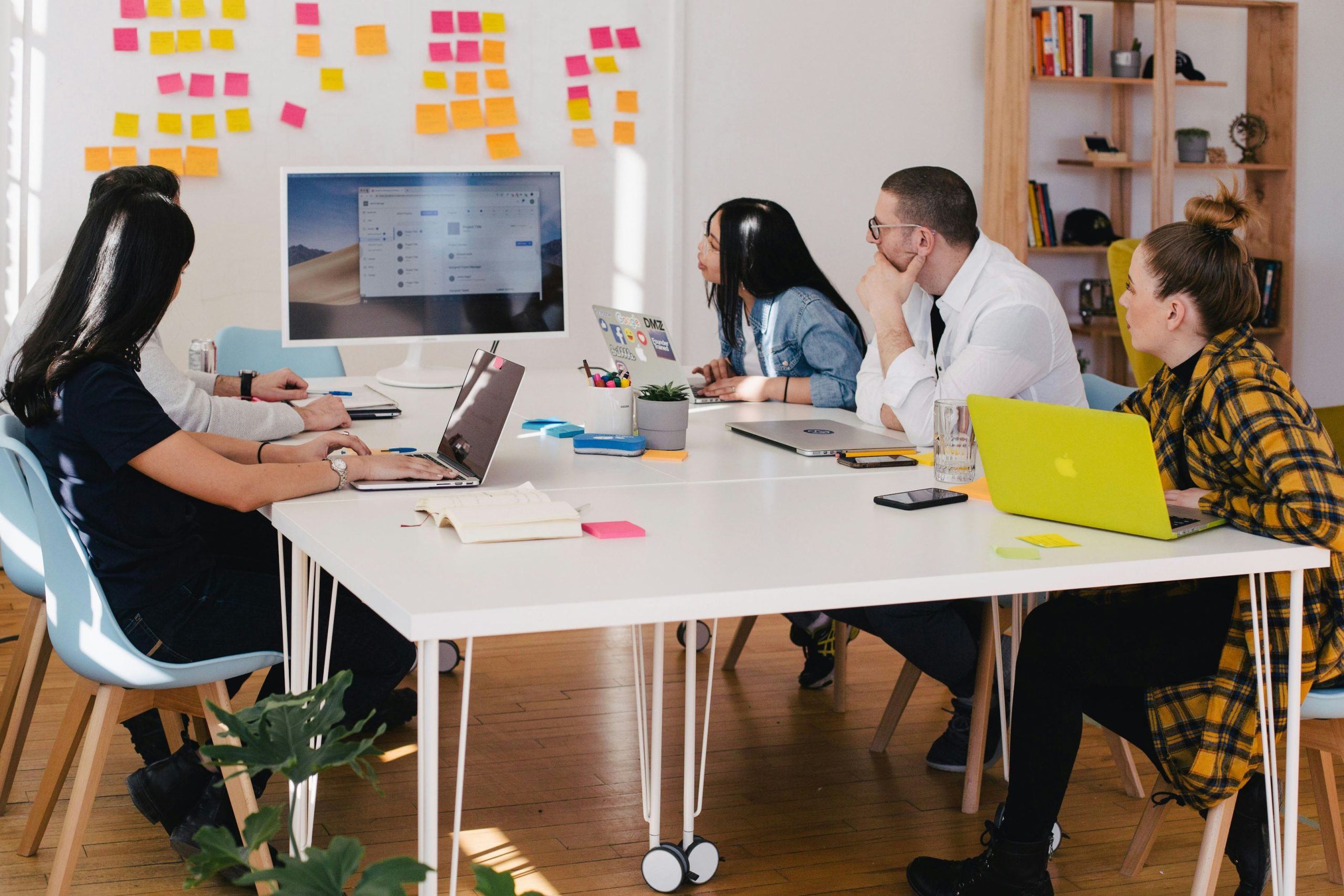 A group of five people sitting down at a desk and looking at a desktop screen.