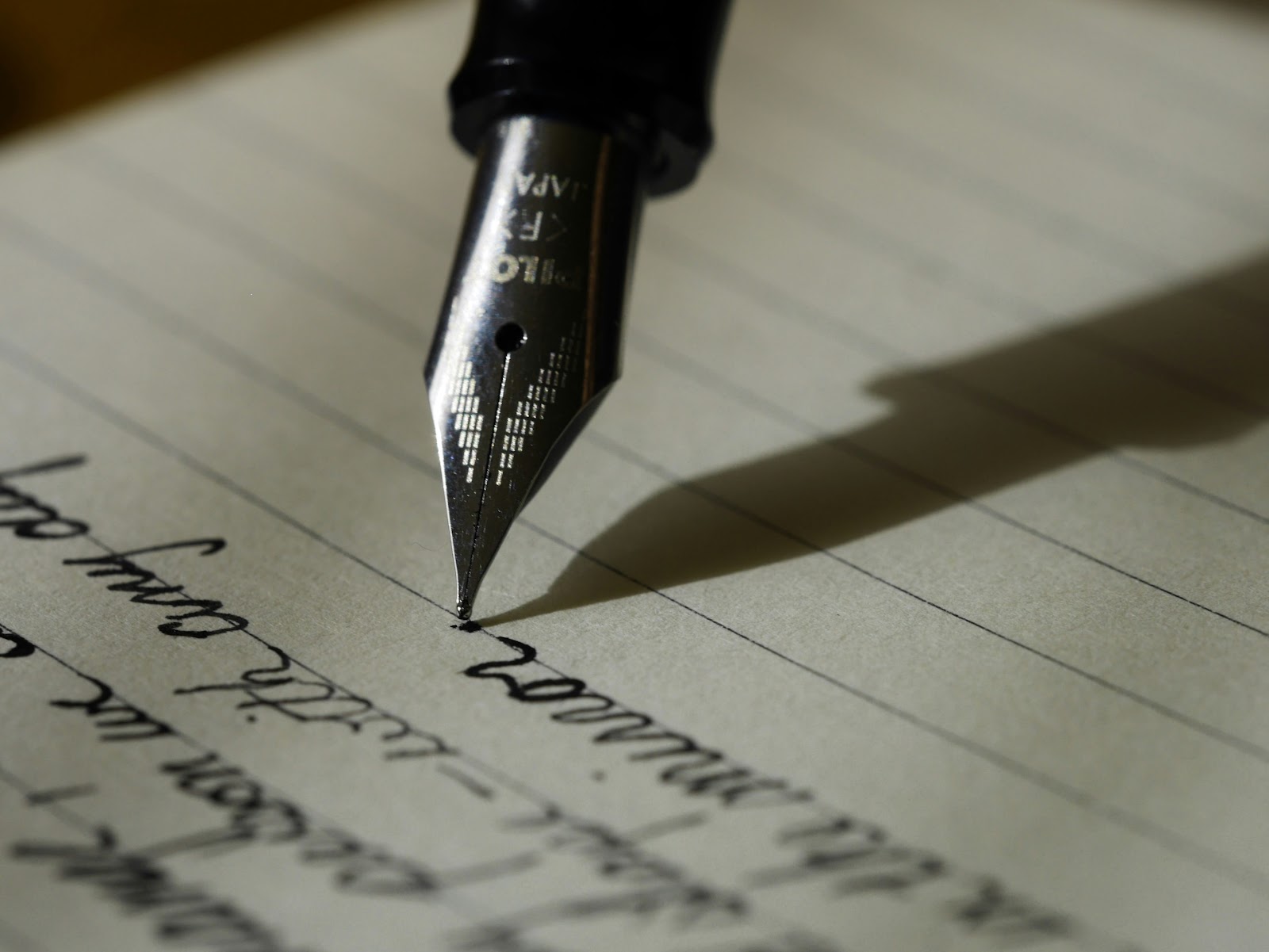 A fountain pen being used to write on lined paper.