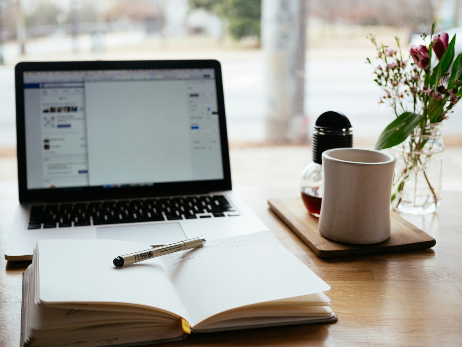 A black laptop next to a notebook, pen, and coffee mug.