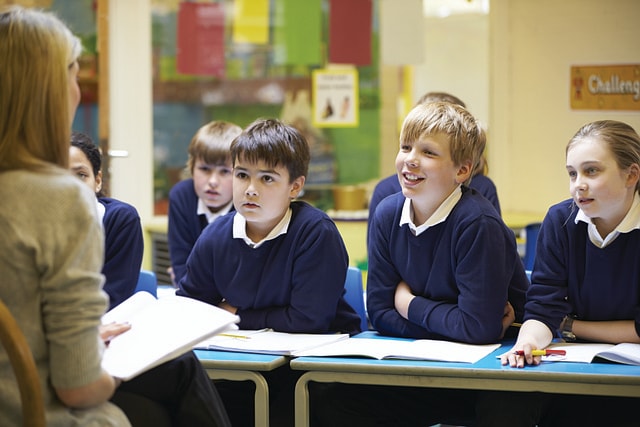 A teacher sitting in front of students and reading a book.