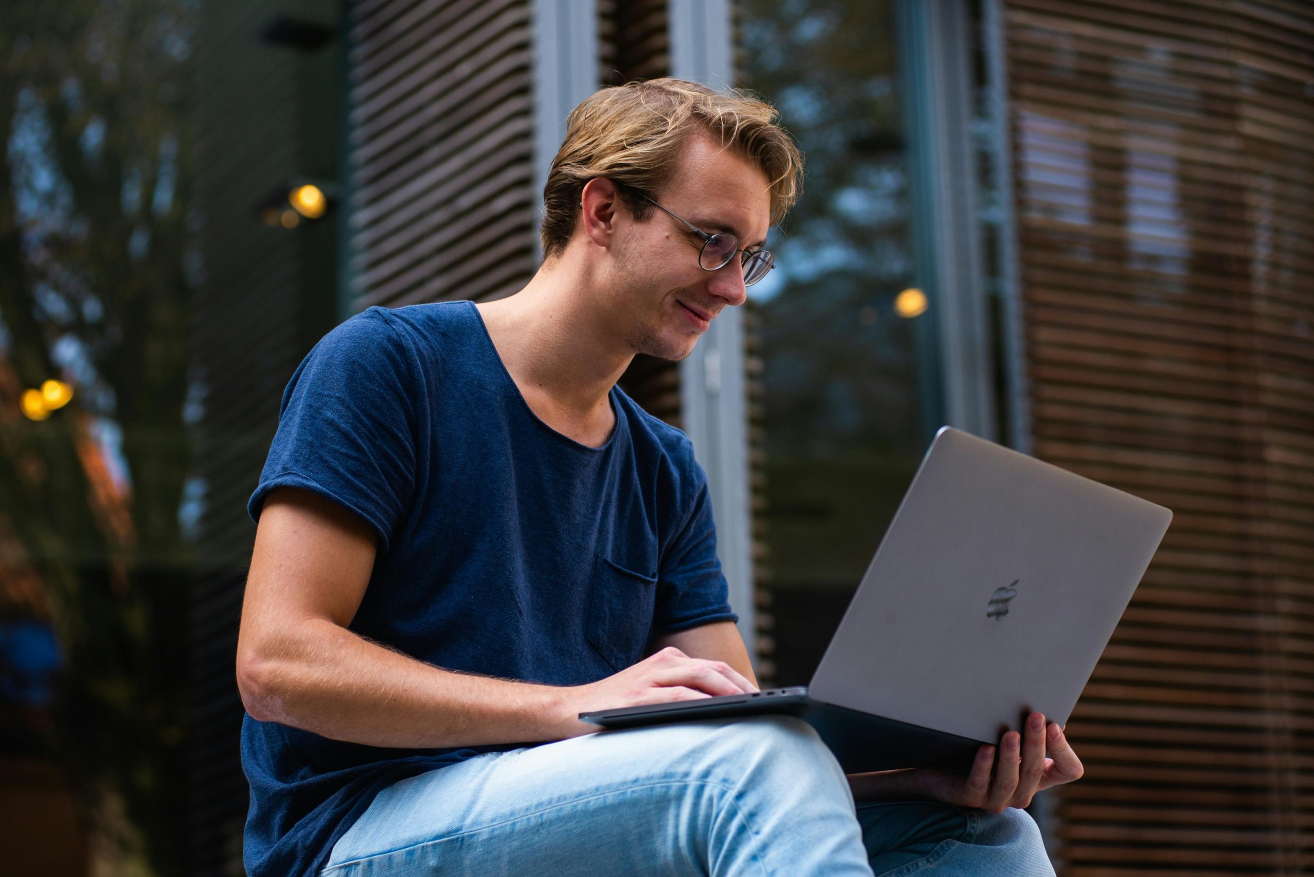 A man sitting in front of his laptop outside on a university campus.