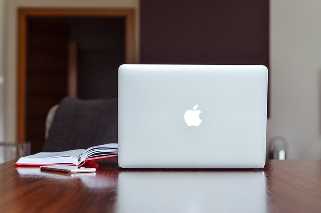 A MacBook and notebook placed next to each other on a wooden desk.