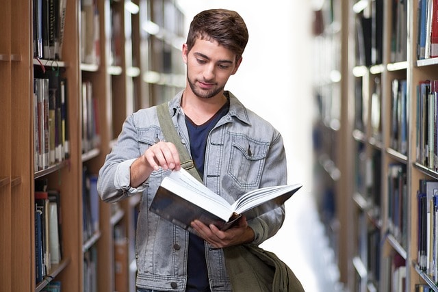 A student standing between two library shelves and reading a book.