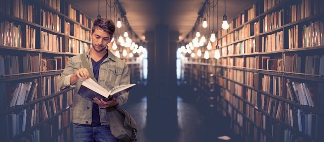 A college student reading a book in between two shelves in a library.