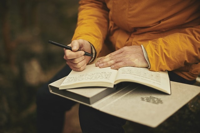 Someone writing in a notebook with a black pen.