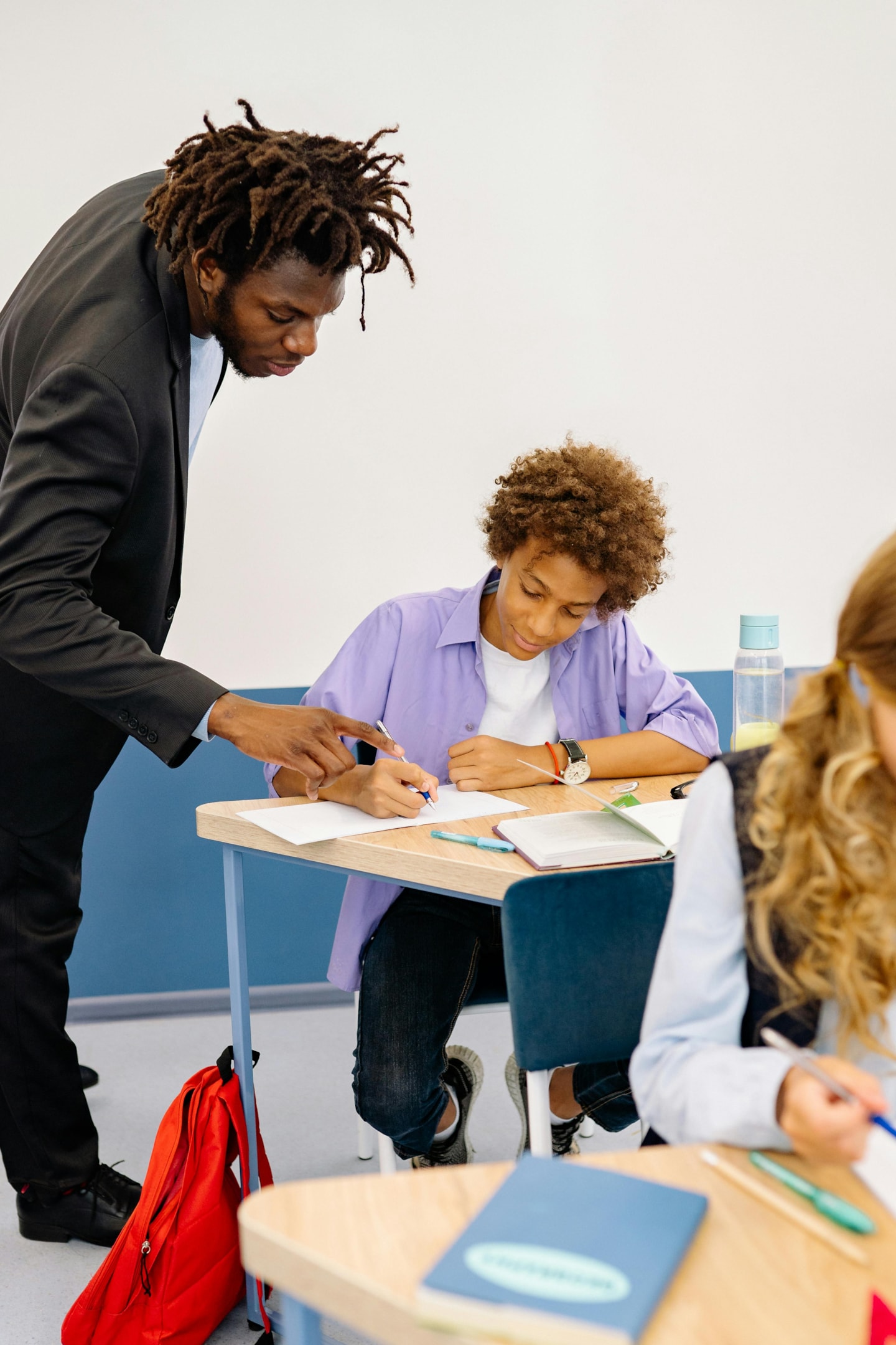 A male teacher is helping a young male student at his desk in school. 