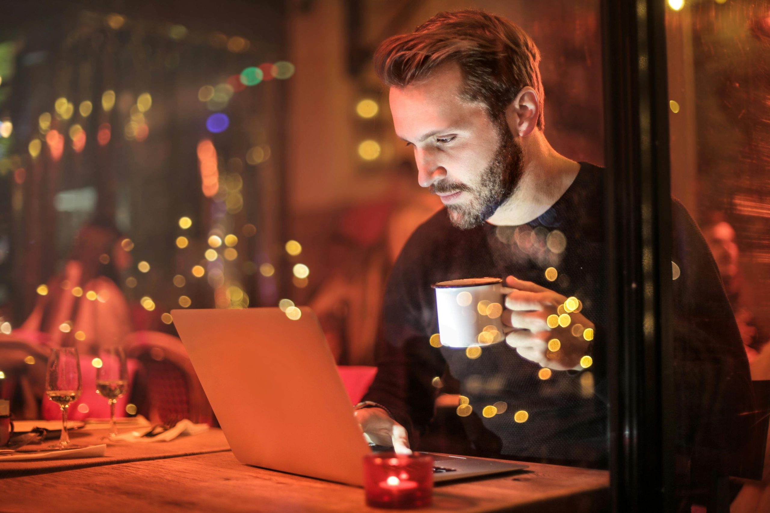 A man holding a mug in front of a laptop in a restaurant.