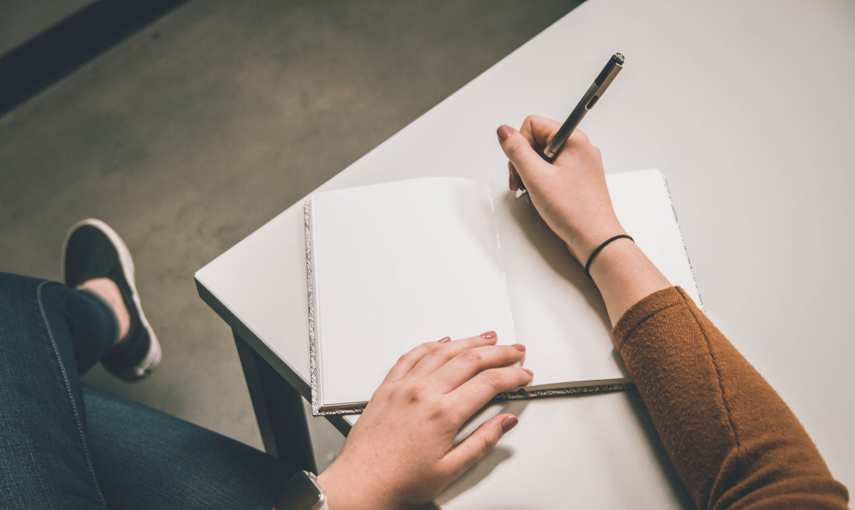 A person writing the best transition words for an essay in a notebook.