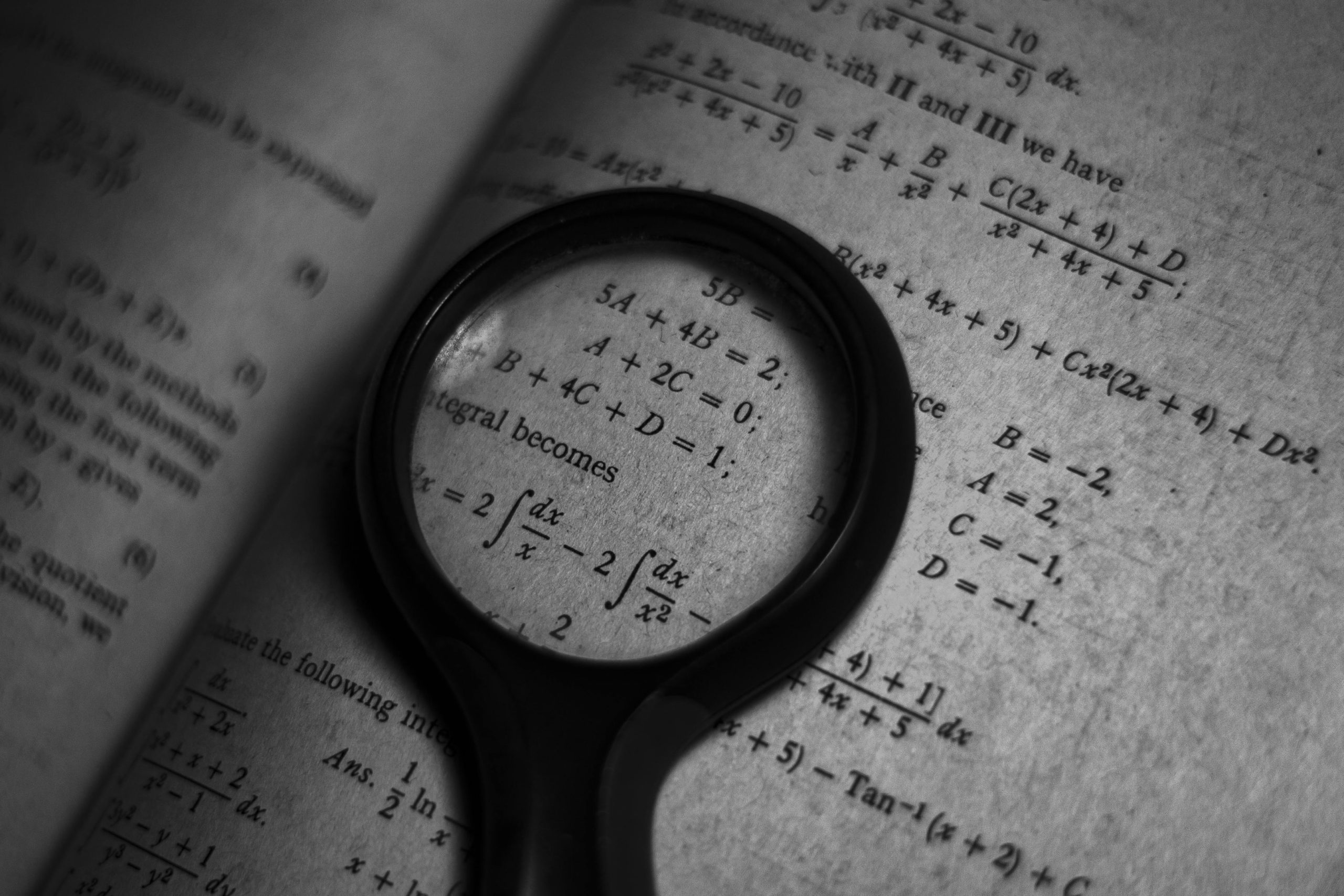 A magnifying glass placed on top of a black and white book with maths equations.